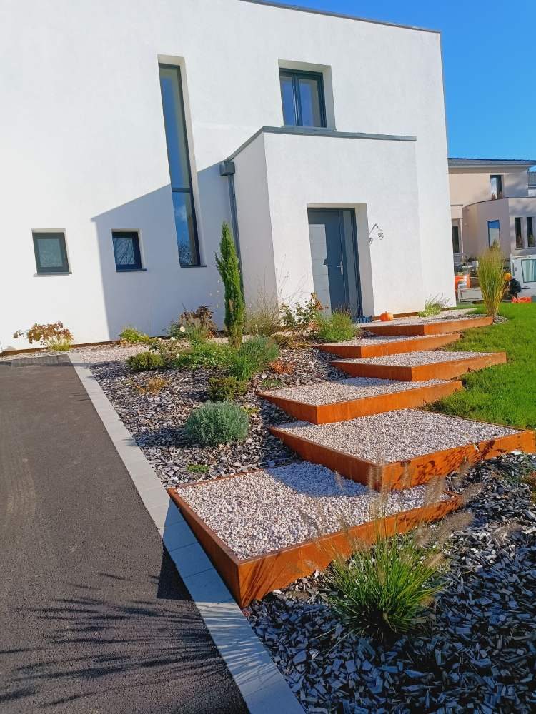 Marches en acier corten et gravier blanc devant une maison contemporaine
