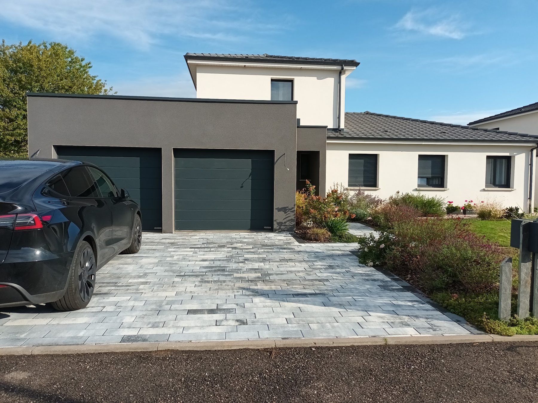 Allée de garage en pavés gris nuancés et massifs fleuris devant une maison